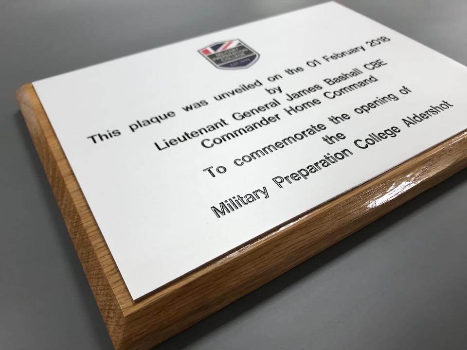 A silver plaque on a wooden backing commemorating the opening of a military prep college.