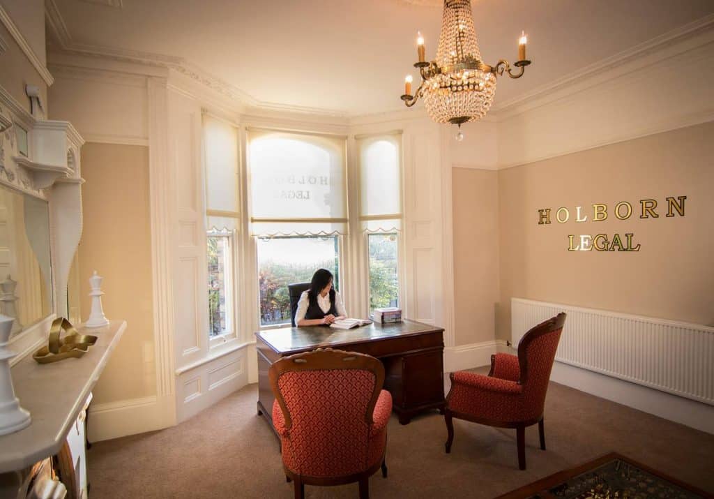 A woman sitting at a desk next to a wall labled Holburn Legal in gold letters.