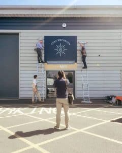 Four people installing a big blue sign over a pair of glass doors.