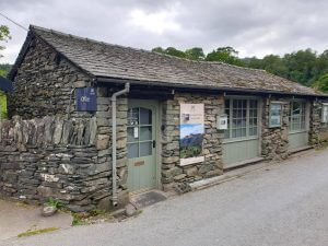 A stone building with a blue sign visible on the side, green doors and window frames, and another sign on the front.