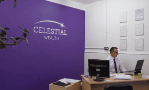 A man sitting at a desk in front of a wall graphic reading "Celestial Wealth".