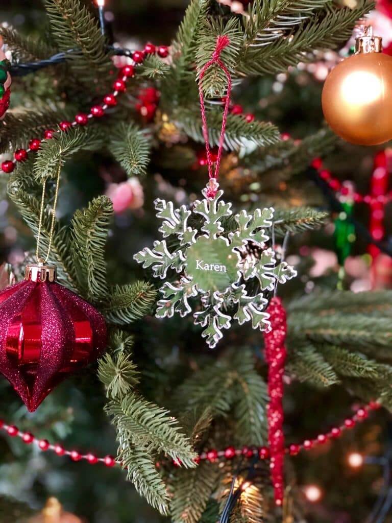 A glass snowflake Christmas ornament on a tree, with "Karen" engraved in the middle.