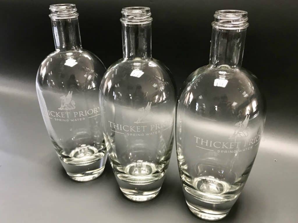 Three glass bottles etched with the Thicket Priory logo.