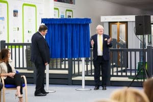 Two men in suits standing before a sign covered by a curtain.