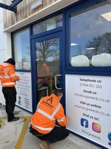 Two men in Andrews branded hi-vis jackets installing signage at Bugweed's.