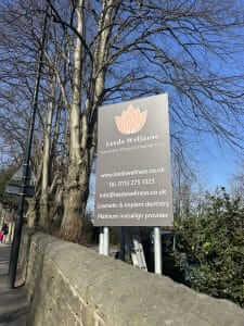 A man in a black Andrews hoodie installing a sign next to a green door.