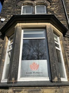 A sign for Leeds Wellness dental clinic standing over a stone wall.
