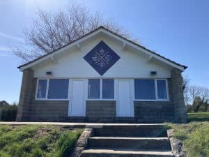 The outside of a cricket pavilion, with a diamond-shaped blue sign.