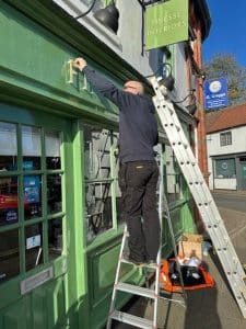A man on a ladder installing a letter F over a shop window.