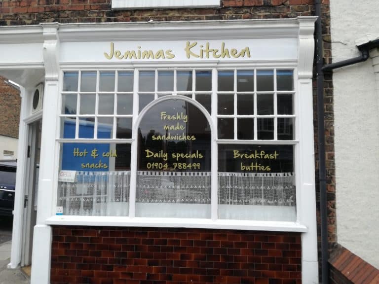 A window with a white sill, with window graphics showing Jemima's Kitchen, their offerings, and their phone number.