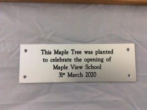 A silver aluminium sign commemorating the planting of a tree.